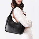 Pebbled--Black Medium | A model holding a u-shaped, flat-bottomed leather shoulder bag with two outside pockets