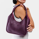 Plum Medium | A model holding a u-shaped, flat-bottomed leather shoulder bag with two outside pockets