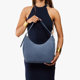 Denim Medium | Model holding u-shaped, flat-bottomed leather shoulder bag with adjustable strap