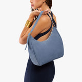 Denim Medium | Model holding u-shaped, flat-bottomed leather shoulder bag with adjustable strap
