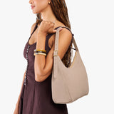 Taupe Medium | Model holding u-shaped, flat-bottomed leather shoulder bag with adjustable strap