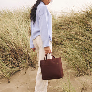 A model holding a Cognac Medium Crossbody walking up a grassy dune.