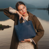 Deep Water | Model holding leather tote bag with front pocket and handles with lake in background