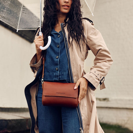 Model holding a transparent umbrella and carrying a Metro Crossbody Bag in Nutmeg