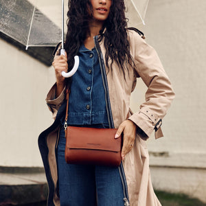 A model holding an umbrella and wearing a Nutmeg Metro Crossbody Bag.