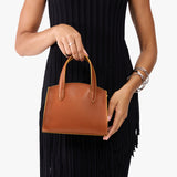 Honey Mini | Model holding small leather tote bag with handles, adjustable crossbody strap, and one back pocket