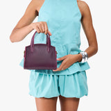 Plum Mini | Model carrying small leather tote bag with handles, adjustable crossbody strap, and one back pocket