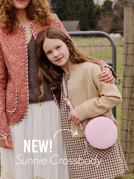 Woman and young girl standing outdoors wearing a pinkaboo Sunnie crossbody bag, featuring 'NEW! Sunnie Crossbody' text.