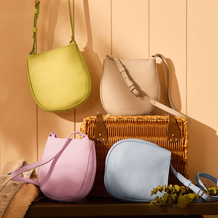 Four Petal Crossbody bags in Shadow Lime, pebbled Bone, Pinkaboo, and Skyway sitting on a bench