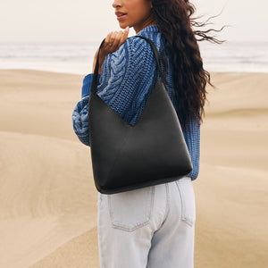 A model standing on the beach wearing a Pebbled Black Naomi Shoulder Bag