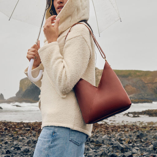 A model standing in the rain holding an umbrella and a nutmeg Naomi Shoulder Bag. featured image