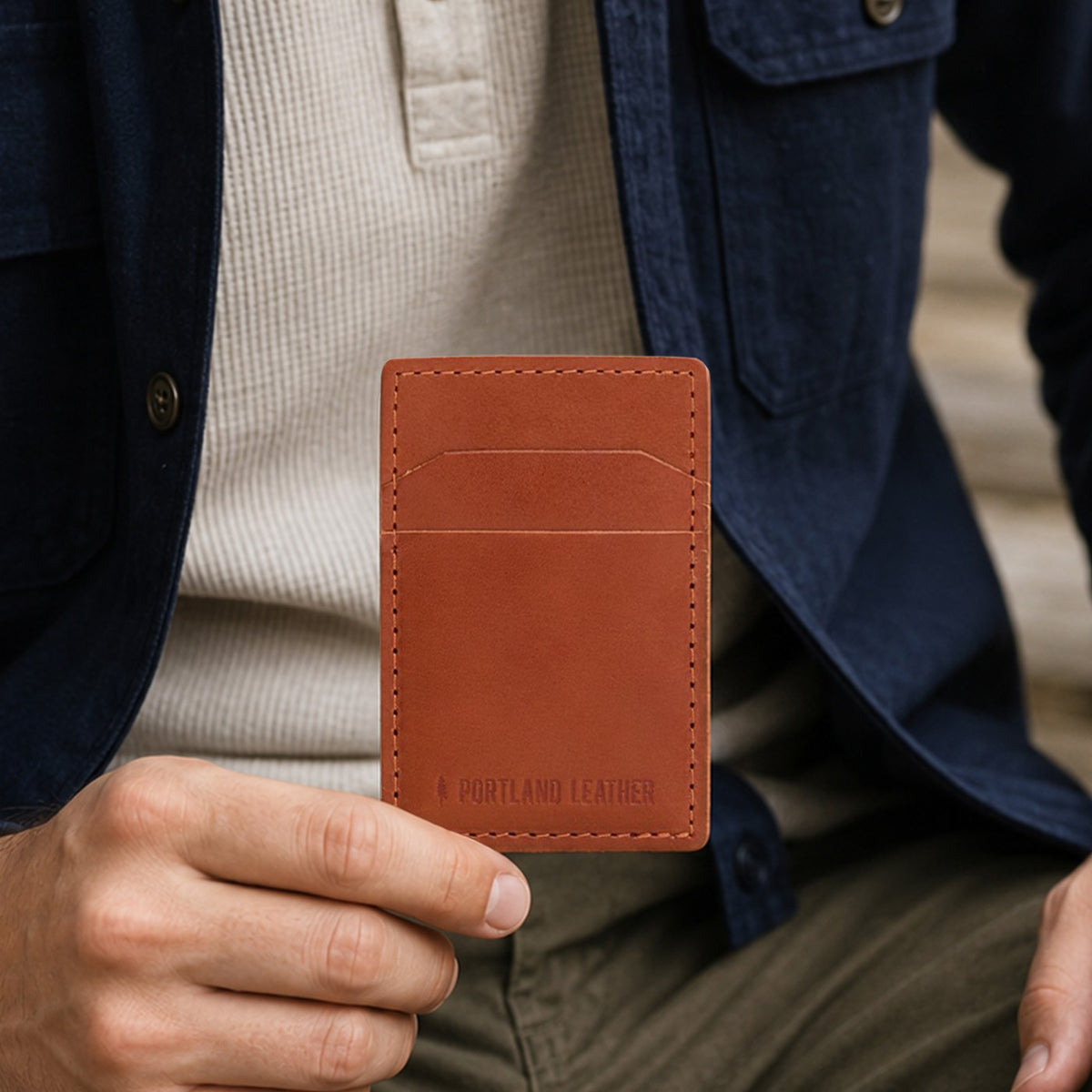 Toscano | A model holds a slim brown leather card holder with two card slots. 