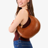 Honey Small | Model carrying crescent shaped leather shoulder bag with zipper closure and adjustable strap