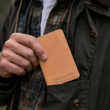 Naturale | A close-up of a model sliding a leather card holder into their shirt pocket