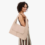 Taupe Large | A model holding a slouchy triangle shaped shoulder bag with a flap