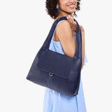 Cobalt Medium | A model holding a slouchy triangle shaped shoulder bag with a flap