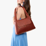 Nutmeg Medium | A model holding a slouchy triangle shaped shoulder bag with a flap