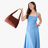 Nutmeg Medium | A model holding a slouchy triangle shaped shoulder bag with a flap