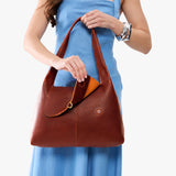 Nutmeg Medium | A model holding a slouchy triangle shaped shoulder bag with a flap
