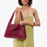 Orchid Medium | A model holding a slouchy triangle shaped shoulder bag with a flap