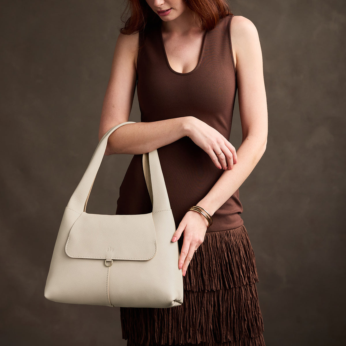 Pebbled Bone*Medium | A model holding a slouchy triangle shaped shoulder bag with a flap