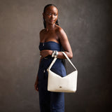 Pebbled Bone Large | Model Wearing medium sized slouchy leather shoulder bag with zipper opening and three metal tree emblems