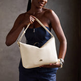 Pebbled Bone Large | Model Wearing medium sized slouchy leather shoulder bag with zipper opening and three metal tree emblems