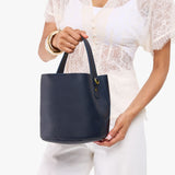 Night Owl Small | Model carrying symmetrical bucket bag with handle, latch closure, and removable crossbody strap