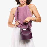 Plum Small | Model wearing symmetrical bucket bag with handle, latch closure, and removable crossbody strap