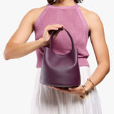 Plum Small | Model holding symmetrical bucket bag with handle, latch closure, and removable crossbody strap