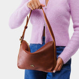 Nutmeg Small | Model holding petite slouchy leather shoulder bag with zipper opening and three metal tree emblems