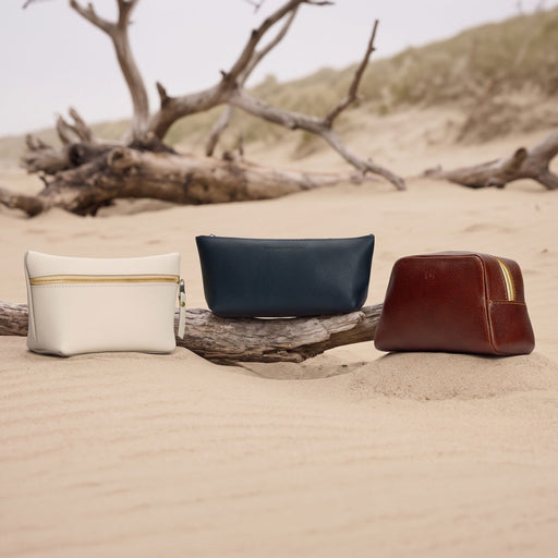 Three makeup bags sitting on the sand and driftwood on a sandy beach. featured image
