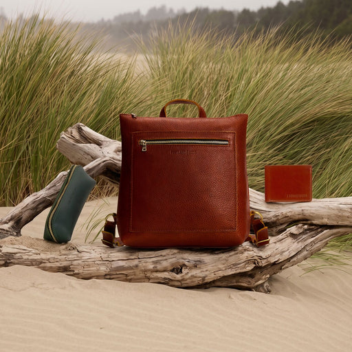 A Tote Backpack, wallet, and Sidekick Pouch resting on driftwood on the beach in front of some tall grass. featured image