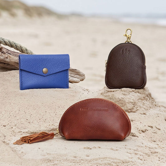 A variety of Small Leather Goods laying in the sand on a beach.