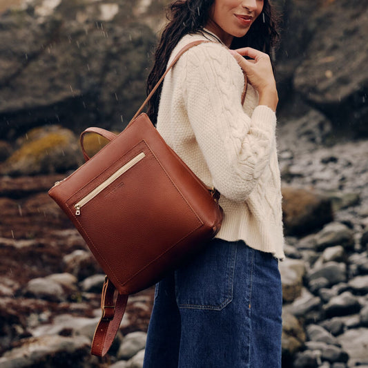 A model carrying a Nutmeg Tote Backpack on a rocky shore in the rain.