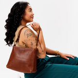 Nutmeg Classic | Model holding leather triangular shoulder bag with zipper top closure and wide shoulder strap