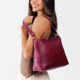 Orchid Small | Model carrying leather triangular shoulder bag with zipper top closure and wide shoulder strap
