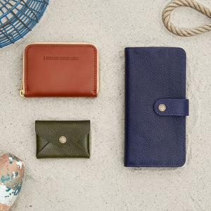 A Small Zip Wallet, Women's Bifold Wallet, Women's Bifold Wallet, and Daisy Plus Wallet laying in the sand around some ocean themed props.